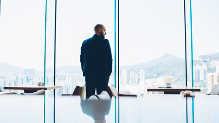 Middle-aged businessman looking outside skyscraper floor-to-ceiling-window