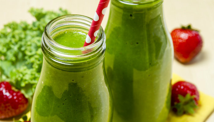 A healthy green smoothie in a glass bottle and red straw with white polka dots
