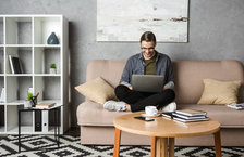 A young man sitting on a couch and working on a laptop from home