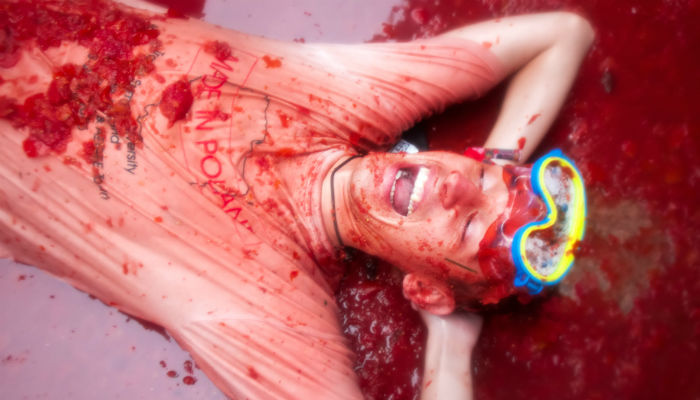 A laughing man wearing goggles and lying in tomato pulp during the La Tomatina festival