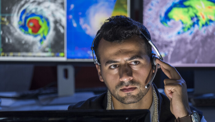 A man sitting at a desk with storms on computer screens behind him