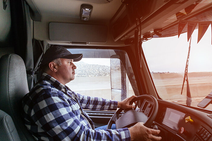Trucker sitting in the cab of a truck on the road.